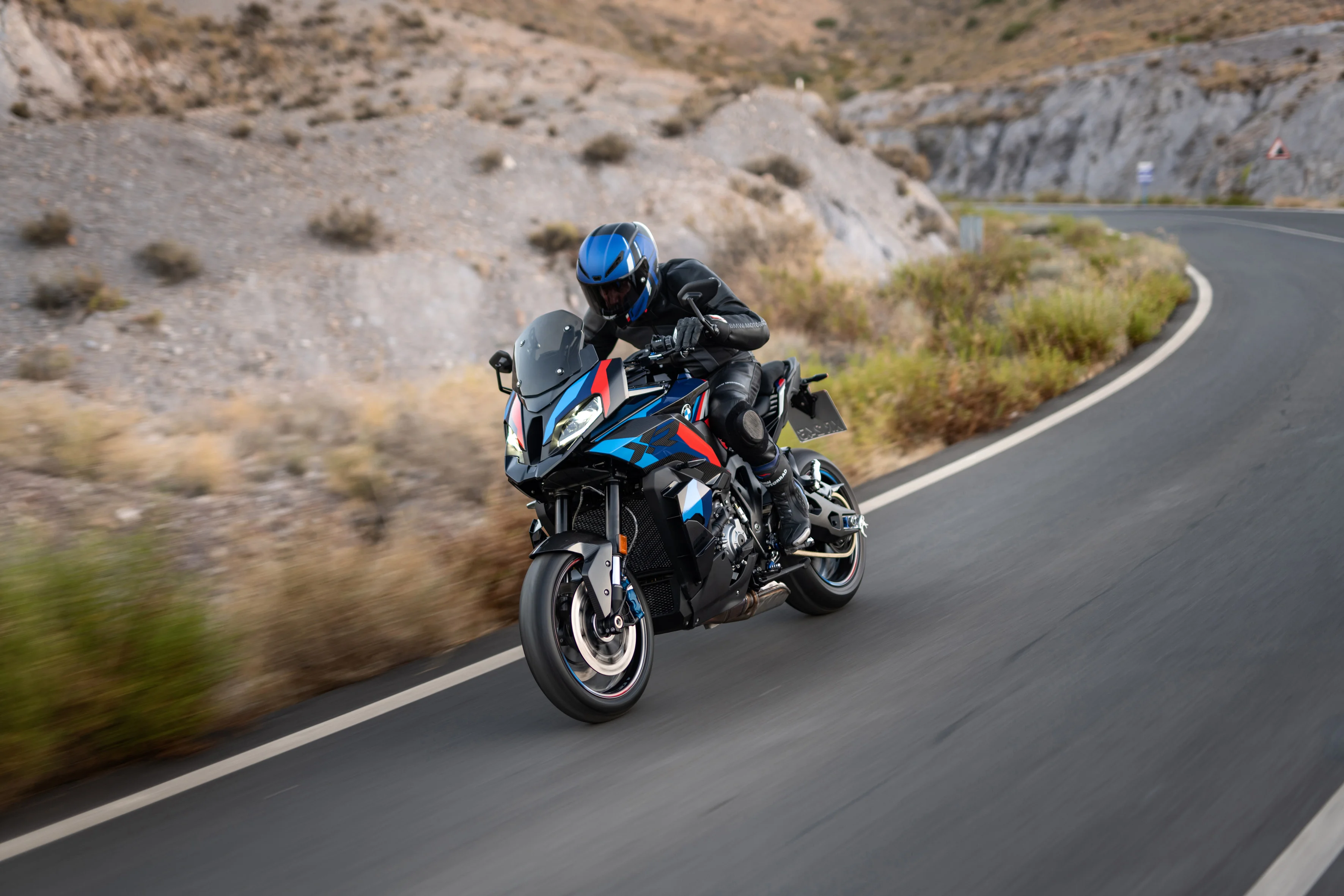 2026 BMW M 1000 XR riding on a mountain road with rocky terrain