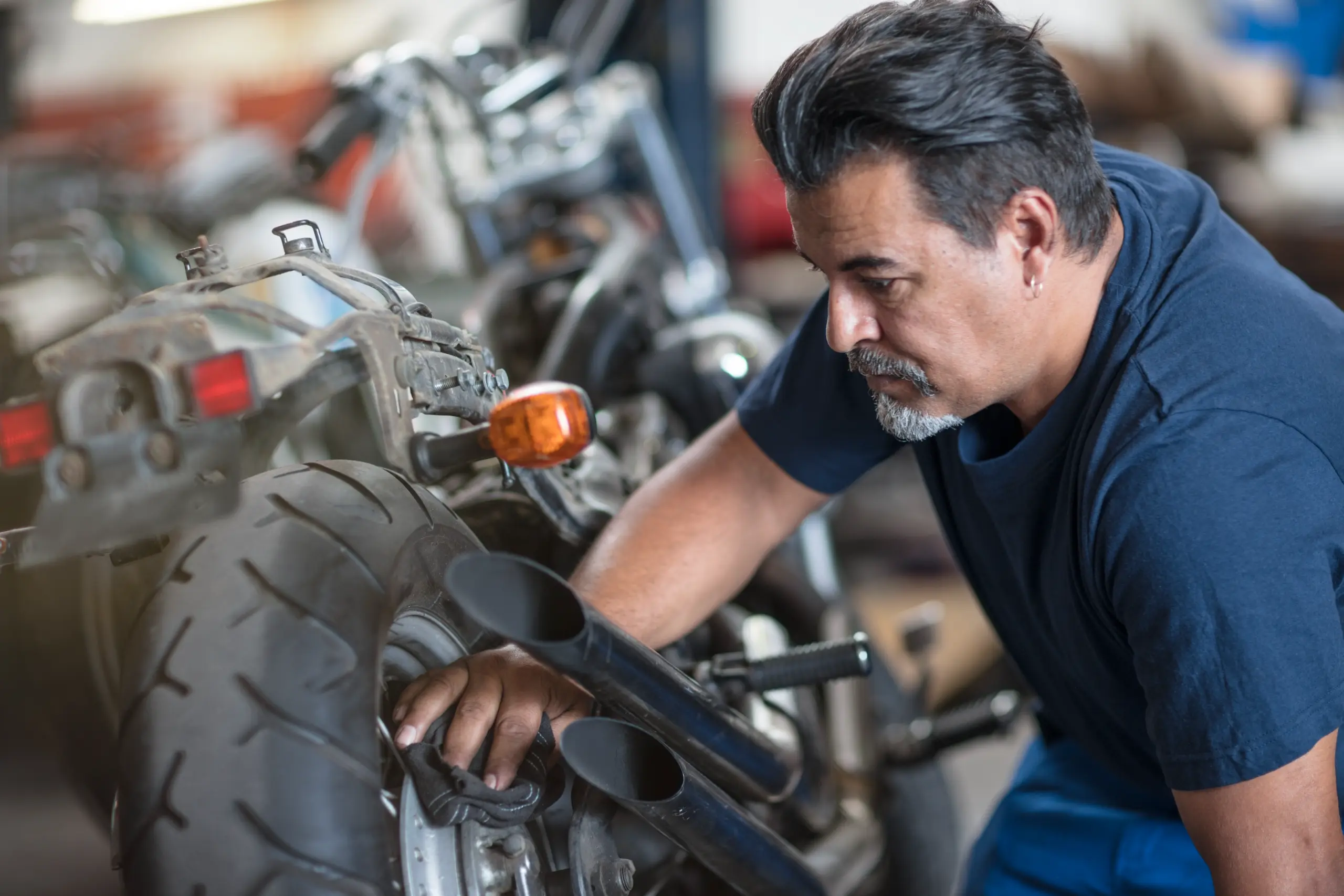Motorcycle mechanic inspecting and servicing the rear wheel in an automotive workshop