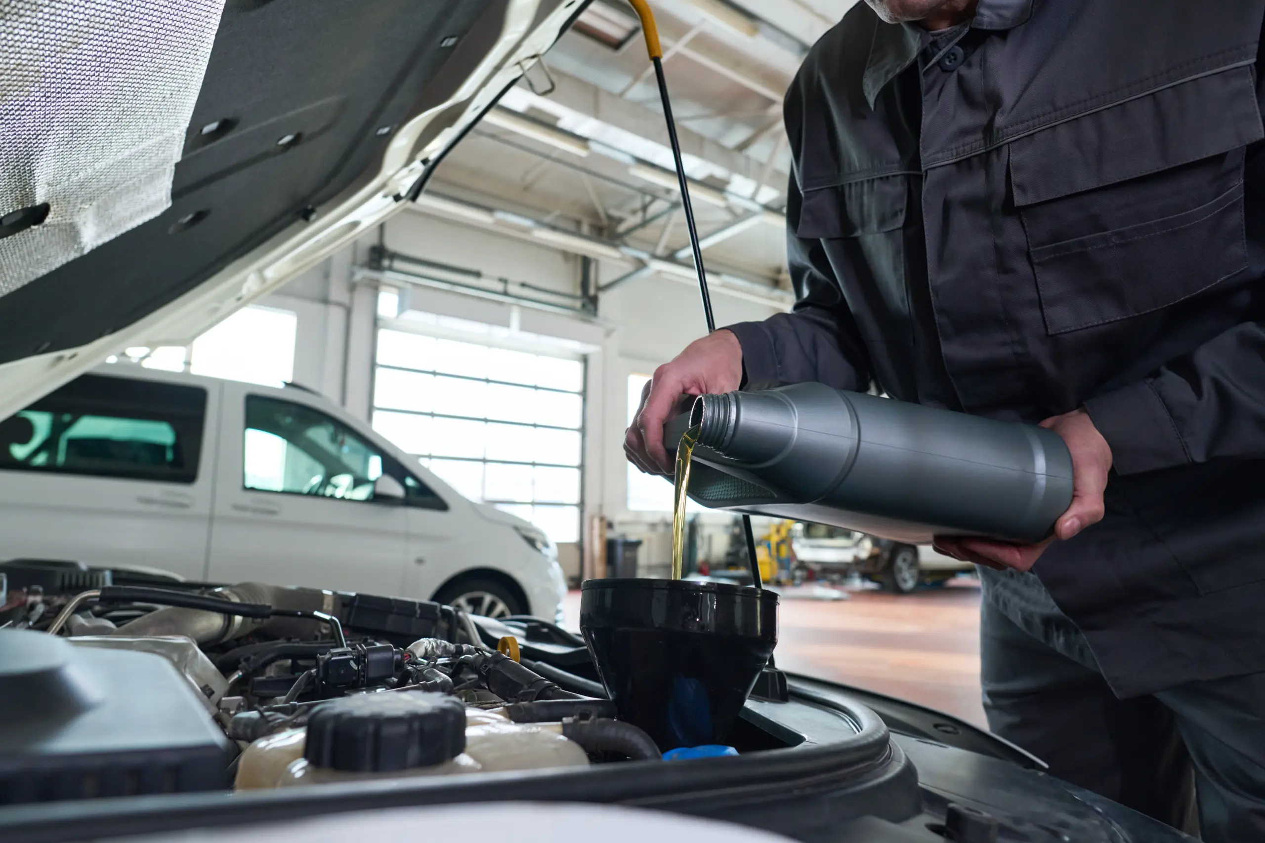 Mechanic pouring fresh motor oil into a vehicle engine during routine automotive maintenance